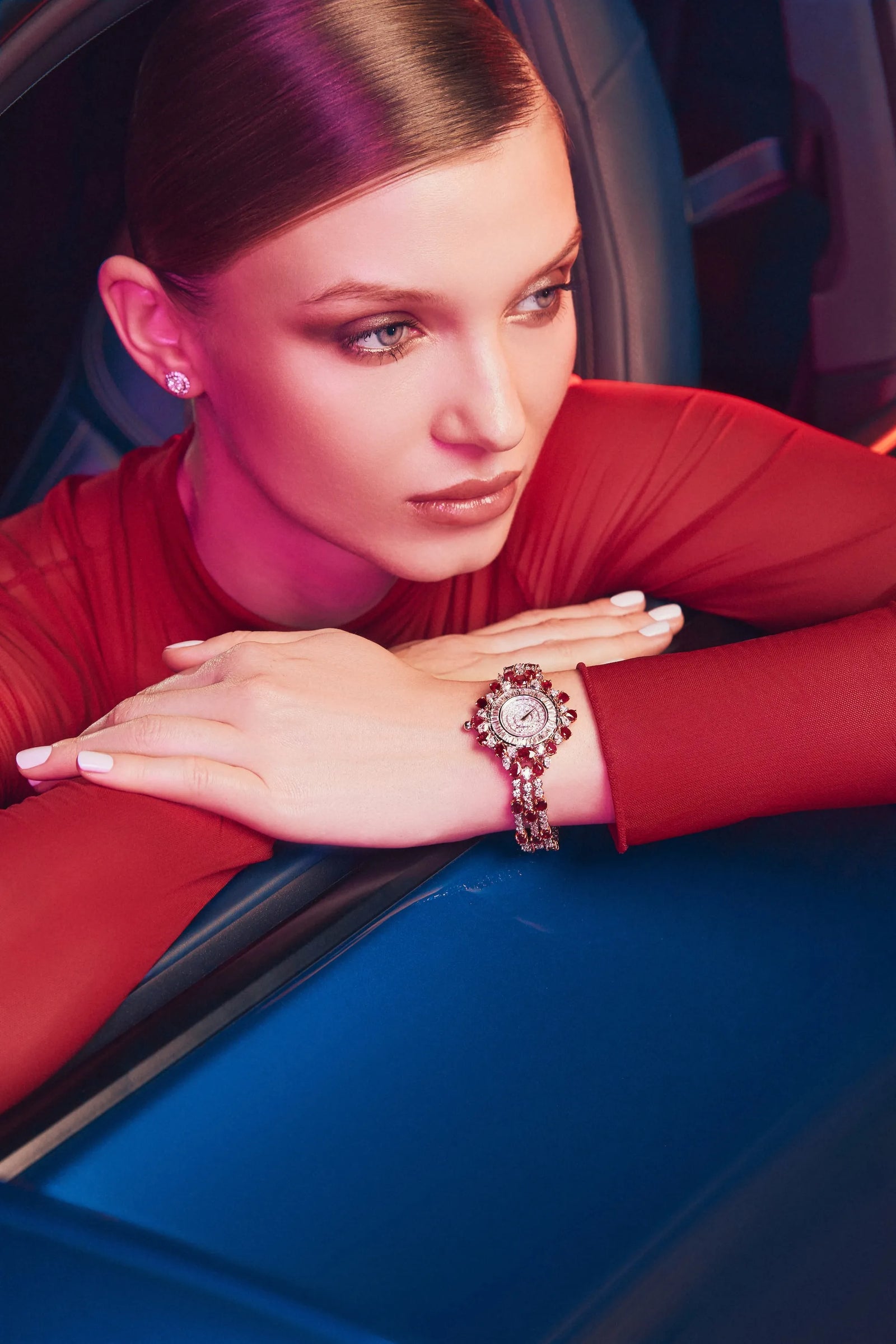 A woman leaning from a car window, a diamond and ruby watch on her wrist