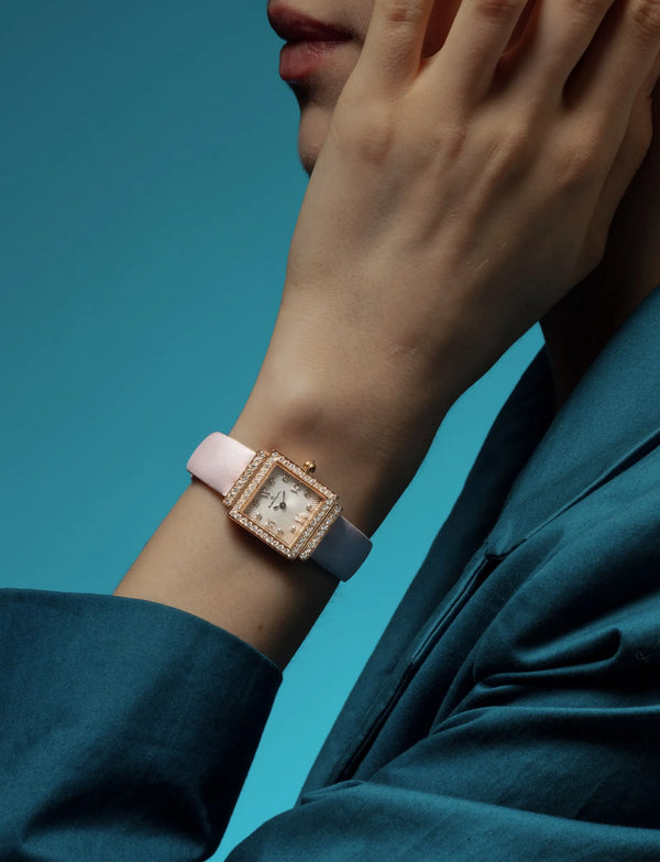 A Gaïa with a diamond bezel and a silvered sunray dial, on a two-tone satin strap, worn against a teal ground