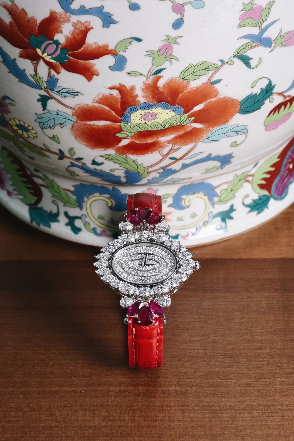 GL.01, an oval diamond dial in marquise diamonds with ruby pear shapes, on a red strap before a porcelain jar